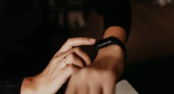 A woman wearing a black fitness tracker on her right wrist. She is using her finger to navigate the watch.